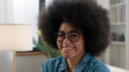 Close up happy positive lady at home laughing portrait female headshot indoors ethnic young millennial African American woman looking at camera smiling laugh at couch dental carefree girl in glassesの写真素材
