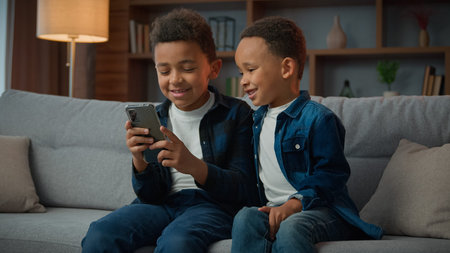 Children gadget addiction two happy laughing African American little boys brothers browsing mobile...