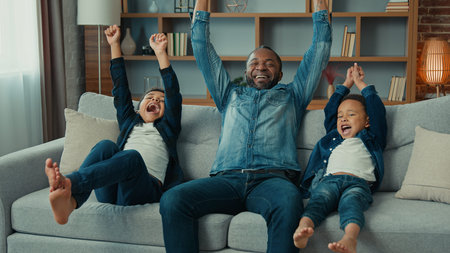 Excited African American happy family father and two siblings boys kids children fans watch TV sport...