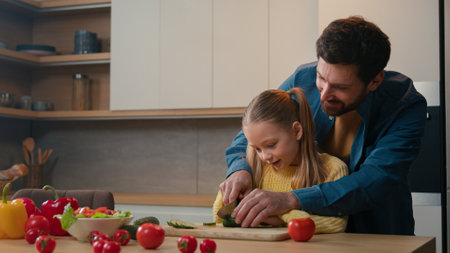 Caucasian father dad help teach show little child girl cute daughter cut vegetables salad cooking together teaching cutting cucumber explain how using knife happy family parental control at kitchenの写真素材