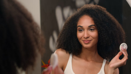 Mirror reflection female washing face with sponge micellar water tonic facial skincare beauty routine African American woman girl with cotton pad wipe wash face remove make-up skin care acne procedureの写真素材