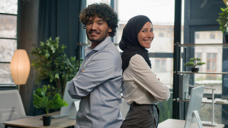 Two happy business partners diverse multiracial colleagues managers entrepreneurs Muslim businesswoman in hijab and Indian latino businessman in corporate office posing crossed hands team partnershipの写真素材