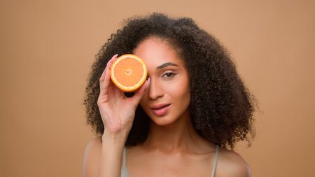 Beauty portrait African American girl woman hold half orange grapefruit dieting vegetarian healthy vitamin summer skin hair care curls fruit natural organic vegan citrus body facial cosmetics productの写真素材