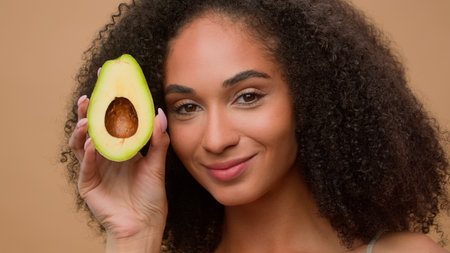 Female portrait studio background smiling African American woman holding fresh healthy avocado face beauty skin care beautiful girl advertising organic natural cosmetics fresh clean facial moisturizeの写真素材
