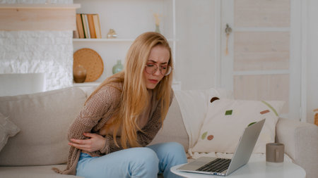 Sick ill girl student business woman unwell lady in glasses Caucasian illness female with laptop at home feeling bad abdomen pain belly ache suffering stomach aching hurt painful menstrual period llyの写真素材