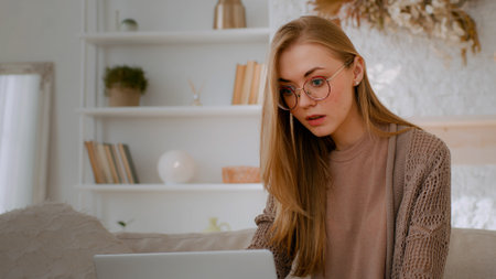 Caucasian shocked woman in glasses looking at laptop reading bad news close mouth with hands holding head with shock failure student girl lost with computer businesswoman worry about business problemの写真素材