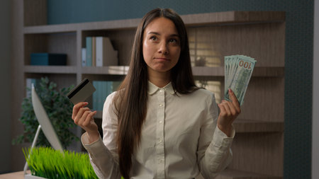Caucasian business girl woman confused puzzled businesswoman choose between credit card and dollars banknotes compare online payment and cash hesitating throw money choosing cashless finance ecommerceの写真素材