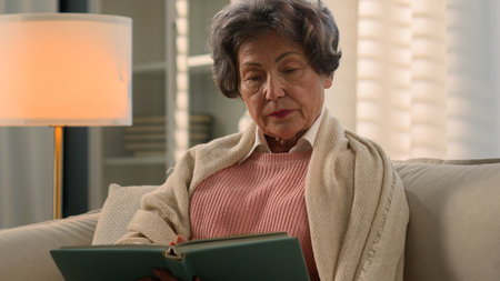 Serious dissatisfied Caucasian old woman senior mature lady covered with blanket calm elderly female retired middle-aged granny grandmother at home couch reading bad book enjoy read novel literatureの写真素材