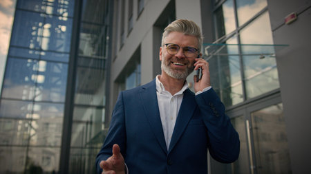 Adult middle-aged businessman walk in city having cell call negotiate senior mature man business investor employer talking mobile phone entrepreneur talk cellphone walking near office company buildingの写真素材