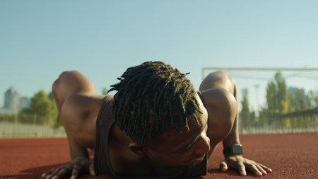 African American man sportsman muscular strong guy bodybuilder do push-ups exercise pumping biceps arms tired male athlete exhausted after workout outdoors on stadium sport health fitness motivationの写真素材