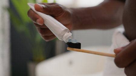 Close up hands squeezing out white toothpaste from tube on toothbrush dental care morning procedure...