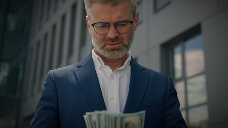 Successful rich wealthy retired employer middle-aged entrepreneur investor old male businessman mature senior man business worker take money cash from pocket counting banknotes dollars finance in cityの写真素材