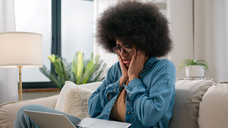 Sad upset shocked anxious worried confused African American woman ethnic girl shock failure lost with laptop bad news computer error mistake refuse notification bank problem exam failing at home sofaの写真素材