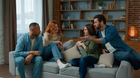Ethnic friends sit on couch in living room diverse colleagues teammates women girls and men guys smiling talk discuss share plans friendly discussion dialogue laugh friendship weekend meeting at homeの写真素材