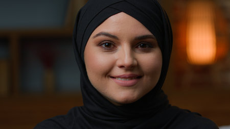 Portrait of Arabian muslim woman in black traditional hijab looking at camera and smiling toothy dental smile. Close up female face islamic turkish girl wear headscarf head shot middle-eastern beautyの写真素材