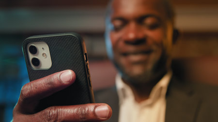 Blurred focus african american businessman holding smartphone browsing social network writing email...