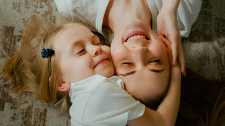 Cute affectionate adopted little kid preschool girl hugging cuddling mother head top view. Child daughter with mum two faces cuddle lying down at home talking smiling with eyes closed tender momentの写真素材