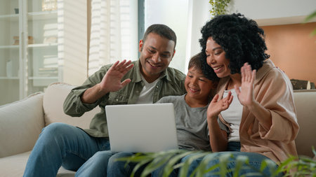 Happy African American family mom dad and teen son use laptop webcam distance video call multiracial parents little boy child wave hands smile greeting relatives remote communication on device at homeの写真素材