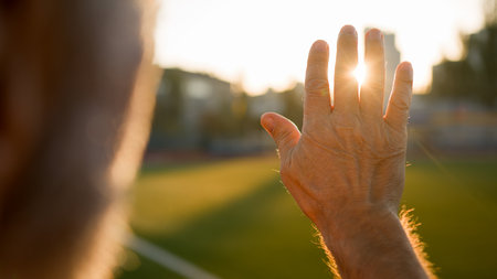 Old man grandfather pensioner looking sunrise sun through palm hand morning close up unrecognizable male stadium city outside physical activity wellbeing healthcare bodycare warm relax freedom natureの写真素材