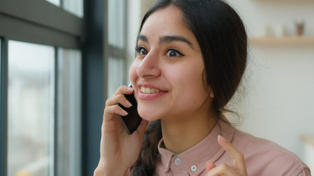 Cheerful laughing Indian Arabian girl gen z student speak mobile phone at office casual carefree...
