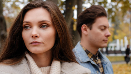 Caucasian girl offended by male lover on background young family couple standing outdoors ignoring...