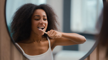Reflection in mirror African American woman holding toothbrush brushing white teeth biracial girl...
