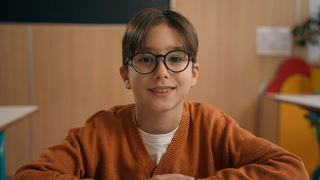Portrait little school boy primary schoolboy Caucasian son kid child guy in glasses eyesight health medicine problem sitting at desk table at class lesson education studying learning study smilingの写真素材