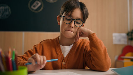 Caucasian thoughtful pensive schoolboy at school looking at textbook reading book education study...