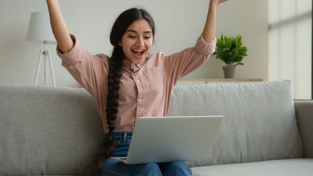 Surprised businesswoman working remote laptop from home office happy Arabian Indian woman girl student studying online winning good exam result celebrate win scream smile achievement business victoryの写真素材