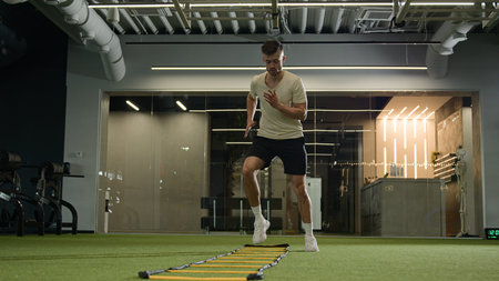 Caucasian sportsman man footballer soccer player training in sports gym exercise with ladder sport...