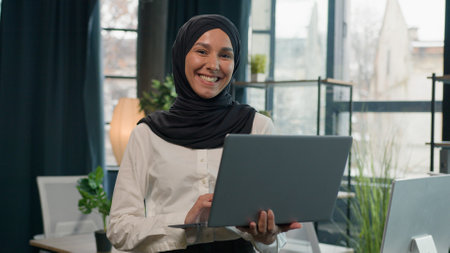 Islam businesswoman in hijab Arabian Indian muslim islamic woman business entrepreneur manager girl with laptop commerce working studying online browsing computer smiling toothy at camera in officeの写真素材