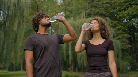 Healthy Indian man Caucasian woman drink in city park outdoor multiracial guy girl happy fitness couple sport people together relax pause break thirst drinking bottled water refresh wellness healthの写真素材