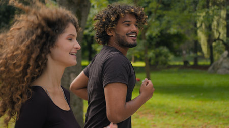 Fitness couple multiracial Caucasian woman and Arabian man running outdoor workout together morning habit two joggers runners athletes jogging in autumn park sport endurance jog run cardio challengeの写真素材