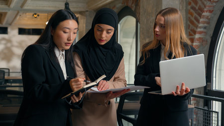 Teamwork multiracial co-workers female multiethnic colleagues girls office partnership Arabian Indian Muslim Asian Caucasian women businesswomen discuss project business laptop papers notes work talkの写真素材