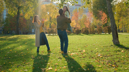 Caucasian happy family weekend holiday nature outdoors in city autumn park together loving father lift little child kid girl daughter spin turning whirl rotate around play fun game mother applaudingの写真素材