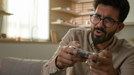 Addicted male gamer Arabian Indian man guy on couch play video game using remote controller joystick...