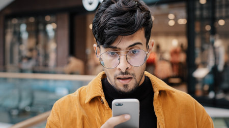 Young guy looking at smartphone screen reading email with great news surprised rejoicing celebrating success winning online game gambling got scholarship invitation to work special offer feeling happyの写真素材