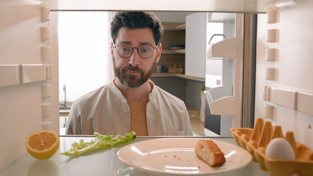 Hungry man guy open empty refrigerator with half lemon lettuce leaf one egg slice of bread leftover...
