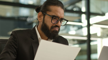 Arabian Muslim business man Indian businessman employer entrepreneur manager confused with papers and laptop in office problem paperwork result talking video call working with documents failureの写真素材