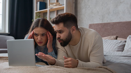 Desperate stressful Caucasian sad couple homeowners confused family wife husband read bad email trouble lost bank mortgage negative result computer failure anxious man and woman lying on bed at homeの写真素材