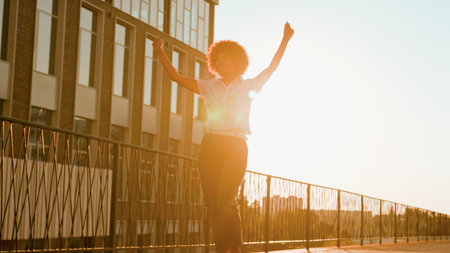 African American happy carefree joyful businesswoman dancing walking in city sun sunshine ethnic cheerful girl female business woman dance walk go outdoors urban celebrate good mood having fun musicの写真素材