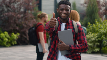 Happy smiling African American student teenager man guy male showing thumb up great cool reaction recommend good education studying enjoy like posing in city university talking multiracial studentsの写真素材