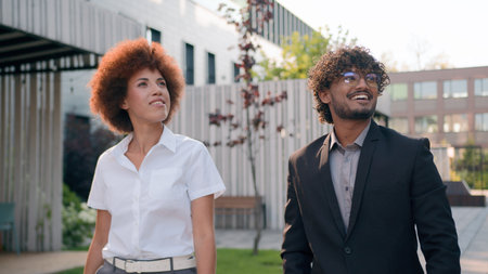 Two diverse multiracial business people walking in city looking around discuss real estate buildings talk walk cooperation teamwork African American woman and Indian Arabian man talking colleaguesの写真素材