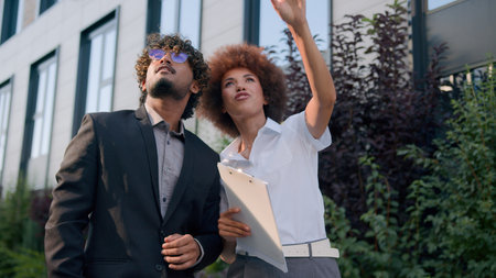 Indian man Arabian businessman investor client and African American woman realtor saleswoman businesswoman talking walking in city looking at modern urban buildings business discussing investmentの写真素材