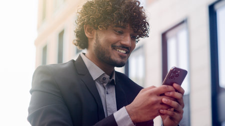 Indian employer Arabian entrepreneur happy amazed cheerful positive businessman using smartphone outdoors in city business man chatting with mobile phone online reading good news corporate successの写真素材