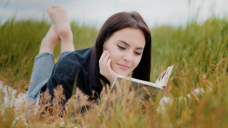 Young serene caucasian brunet woman girl lying on grass outdoors attractive smiling teenage student reads book enjoy romantic literature history relax outside spend time cultural leisure lazy weekendsの写真素材