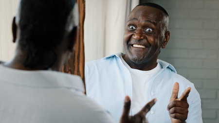 Close up senior comical man look in mirror reflection african american retiree confident 50s unshaven emotional adult businessman pointing forefinger at himself smiling toothy make facial wow reactionの写真素材