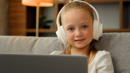 Lovely happy child pretty girl in headphones sit at apartment listen music on laptop playing...