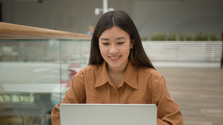 Female office employee Asian woman open laptop in cafe start online job with computer smiling ethnic...