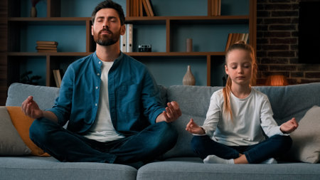 Peaceful caucasian family young father man with daughter little girl kid child sit in lotus pose meditate practice yoga together at home health exercise feel calmness no stress harmony body balanceの写真素材